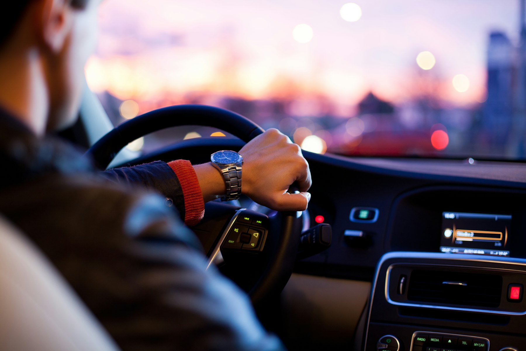 Driver's hand on a steering wheel at dusk