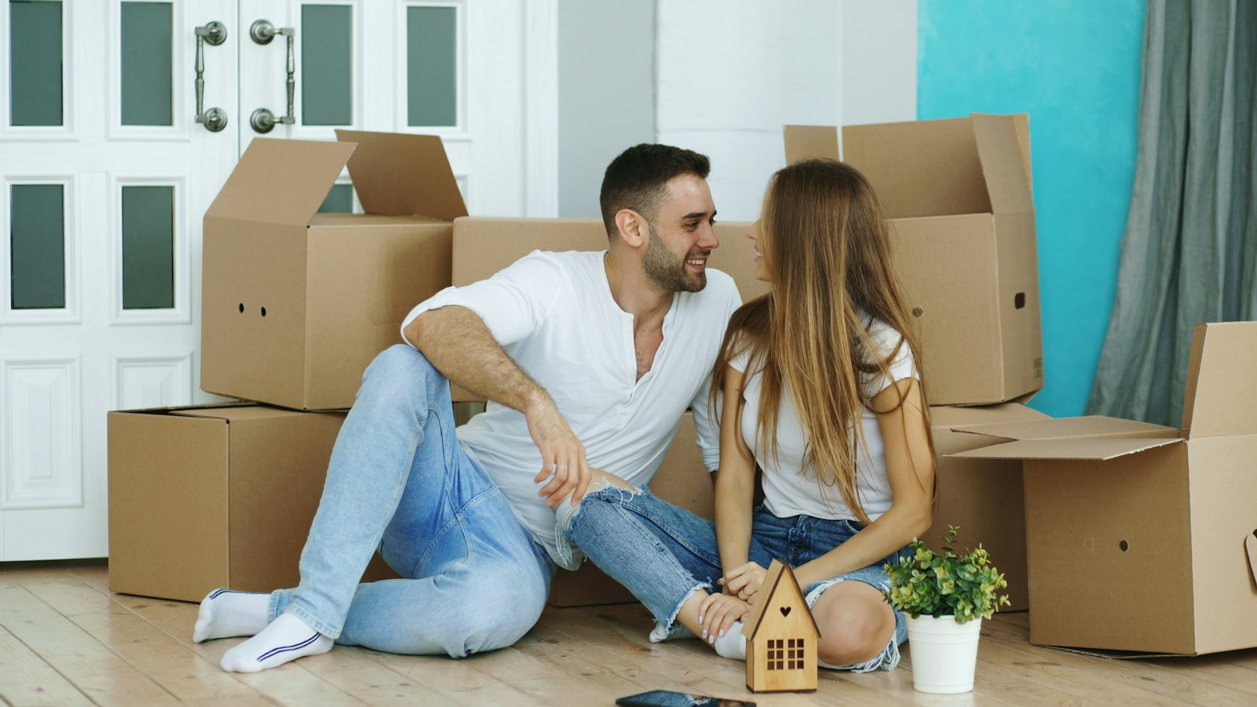 Couple seated on the floor surrounded by moving boxes in a new home